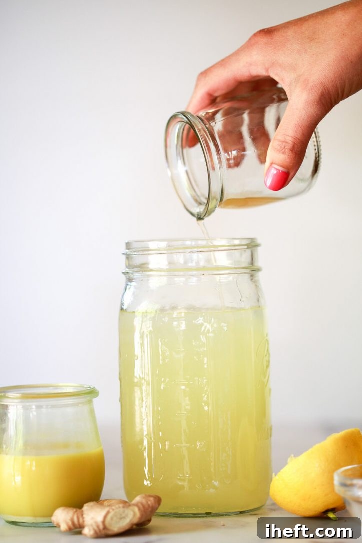 Apple cider vinegar is poured into a quart sized jar with ginger juice and lemons on the side. 