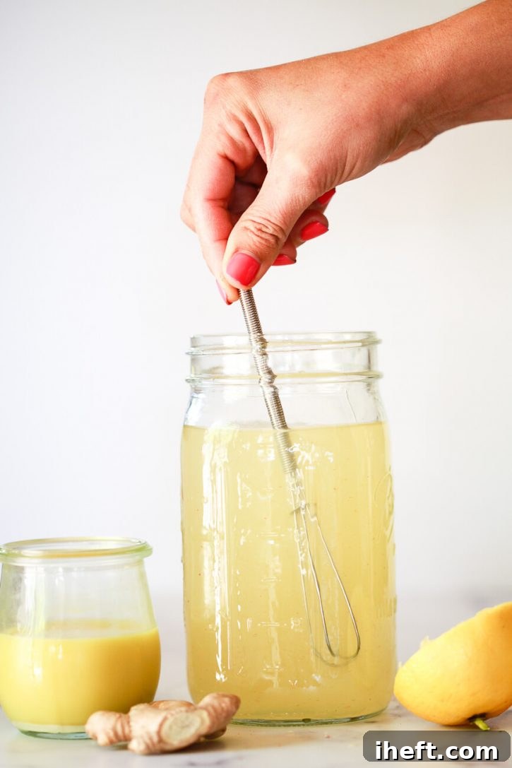 A hand whisks together a lemon ginger apple cider vinegar cleanse detox drink. 