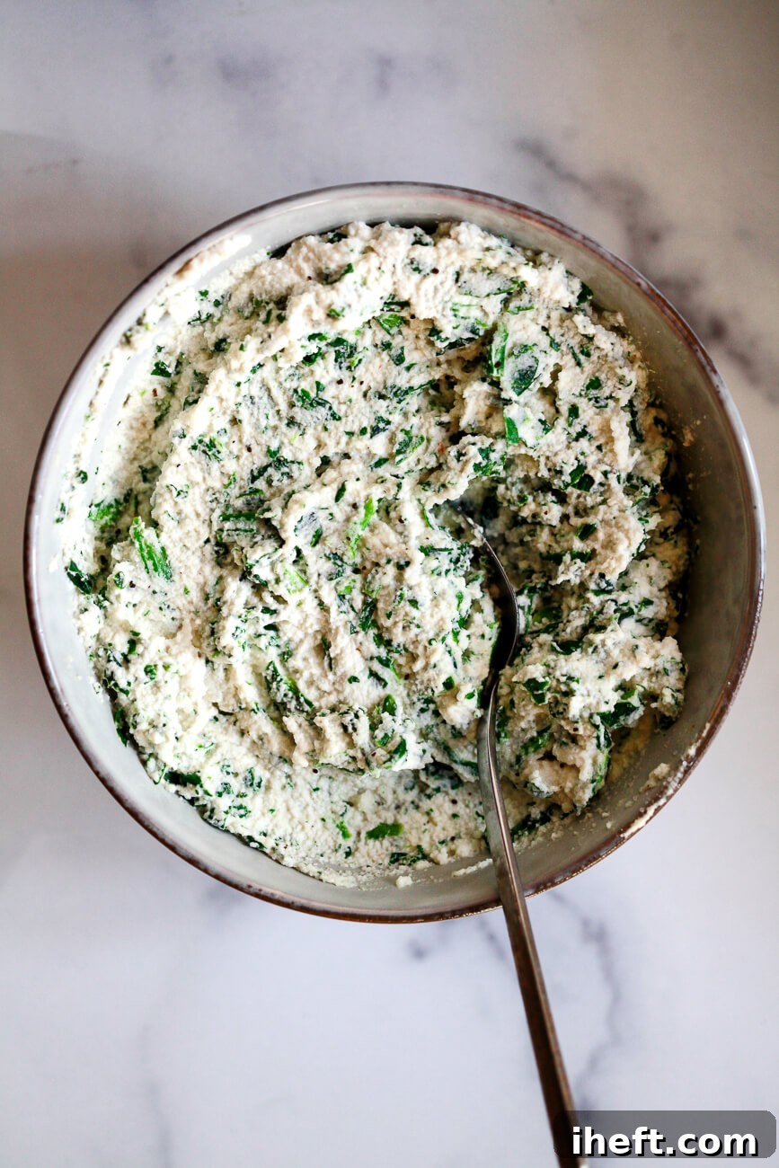 A bowl of ricotta and spinach mixed together with a spoon to make the filling for ricotta stuffed shells. 