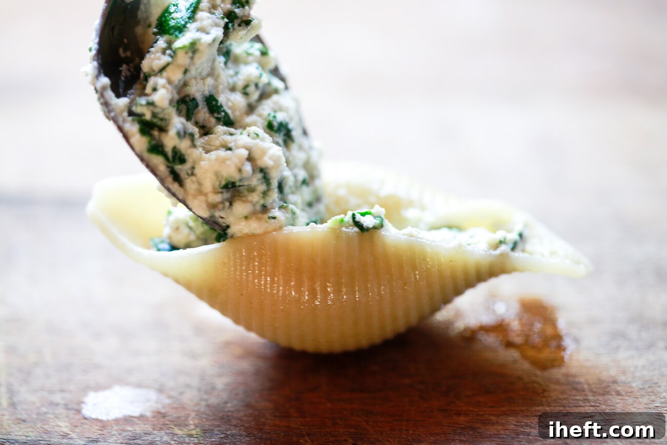 A close-up photo of a spoon filling a cooked Conchiglioni pasta shell with spinach ricotta filling. 