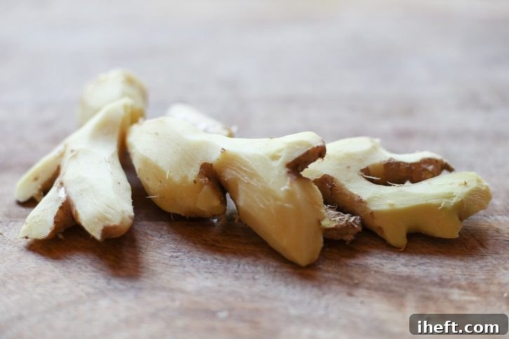 A close-up photo shows fresh ginger root, carefully peeled and ready for grating, resting on a clean wooden cutting board, illustrating the first step in manual ginger juice extraction.