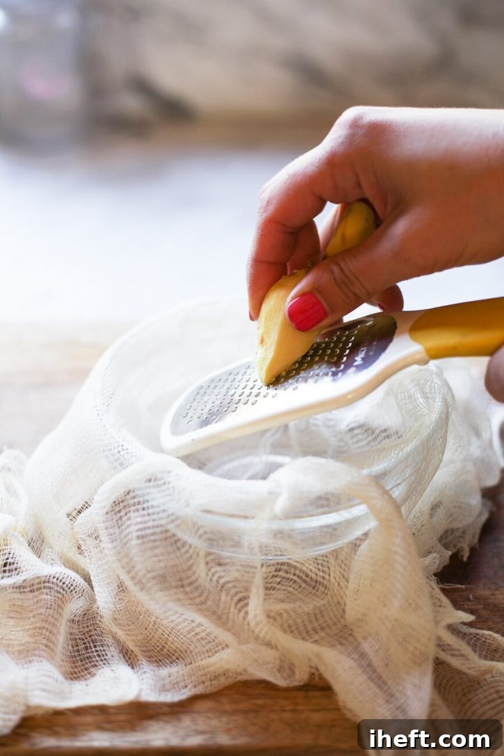 A peeled piece of ginger is meticulously grated with a Microplane into a cheesecloth-lined bowl, demonstrating the technique for making ginger juice without a juicer or blender.