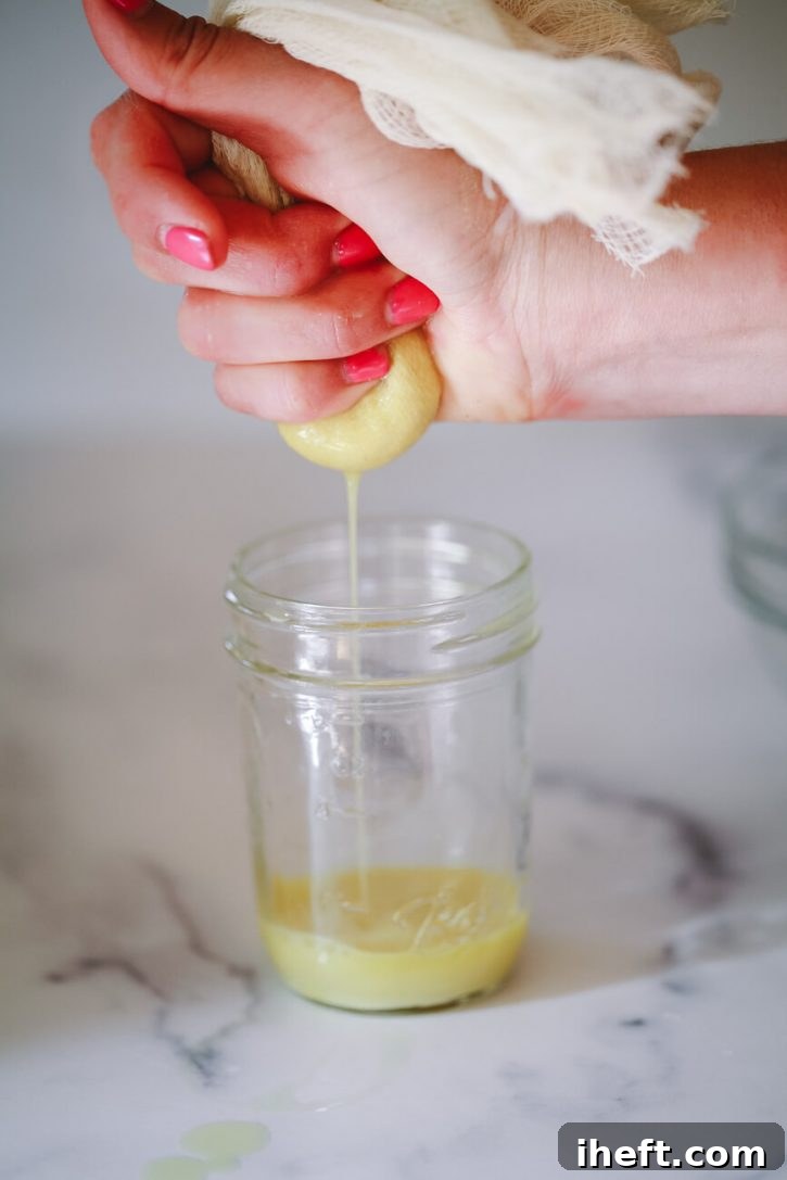 Fresh ginger juice is expertly squeezed through a piece of cheesecloth, held above a small collection jar, clearly illustrating the final step in making ginger juice manually without a juicer.