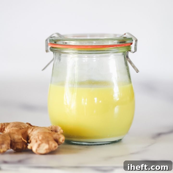A beautifully presented shot glass filled with golden ginger juice, garnished with a slice of fresh ginger and a mint leaf, embodying the vibrant health benefits of this homemade elixir.