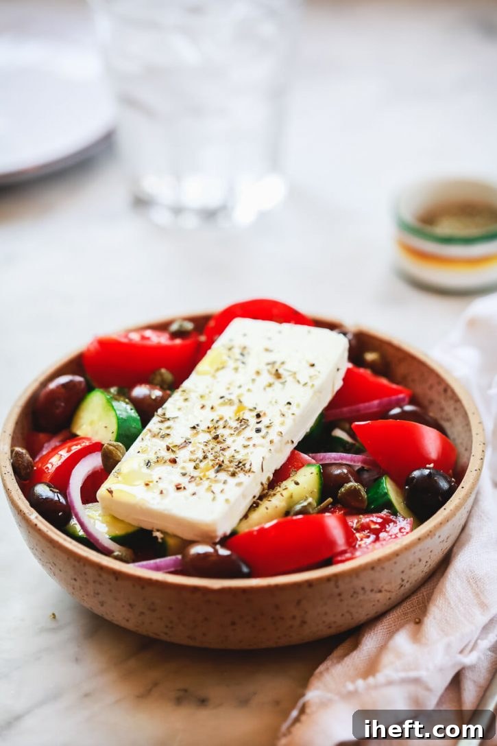 A beautifully arranged bowl filled with traditional Greek village salad, showcasing ripe red tomatoes, crisp cucumber, purple onion slices, glossy Kalamata olives, and a generous slab of authentic feta cheese, all glistening with olive oil.