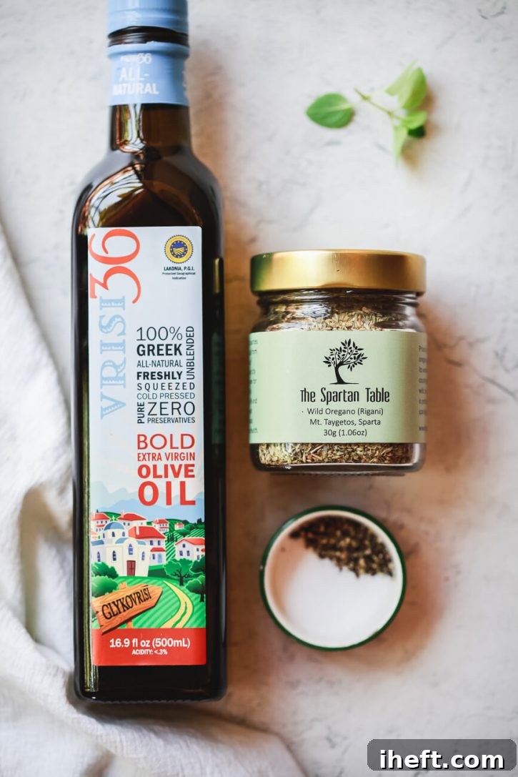 An overhead shot showcasing the minimalist dressing ingredients for traditional Greek salad: a bottle of premium Greek extra virgin olive oil, a small bowl of dried Greek oregano, and a pinch of flaky sea salt on a marble countertop.