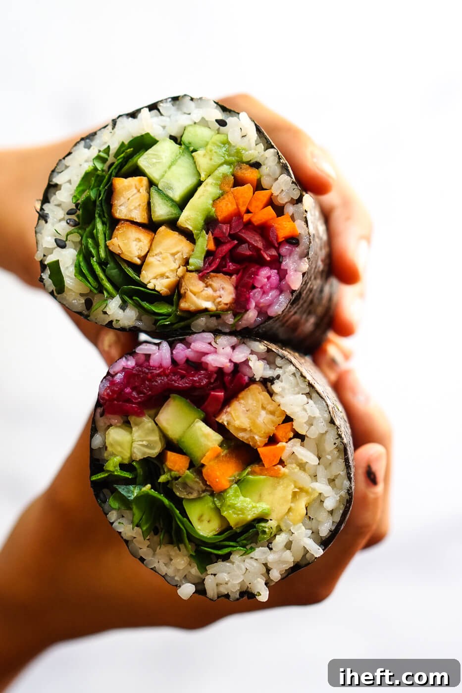 Photograph of hands holding two halves of a sushi burrito filled with vegetables and tempeh.