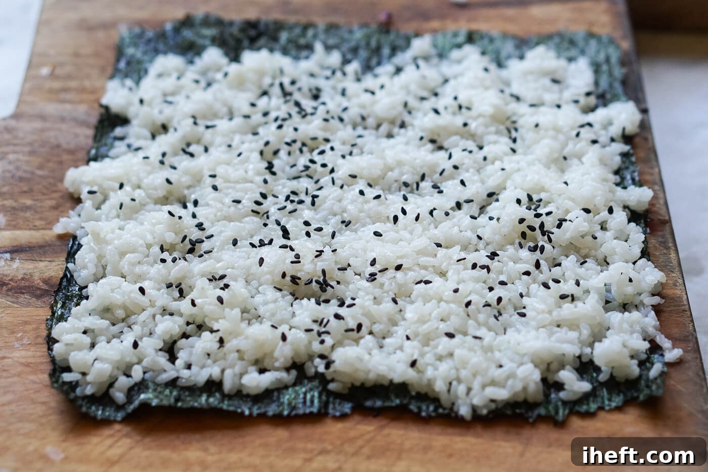A piece of nori is topped with sushi rice and black sesame seeds.