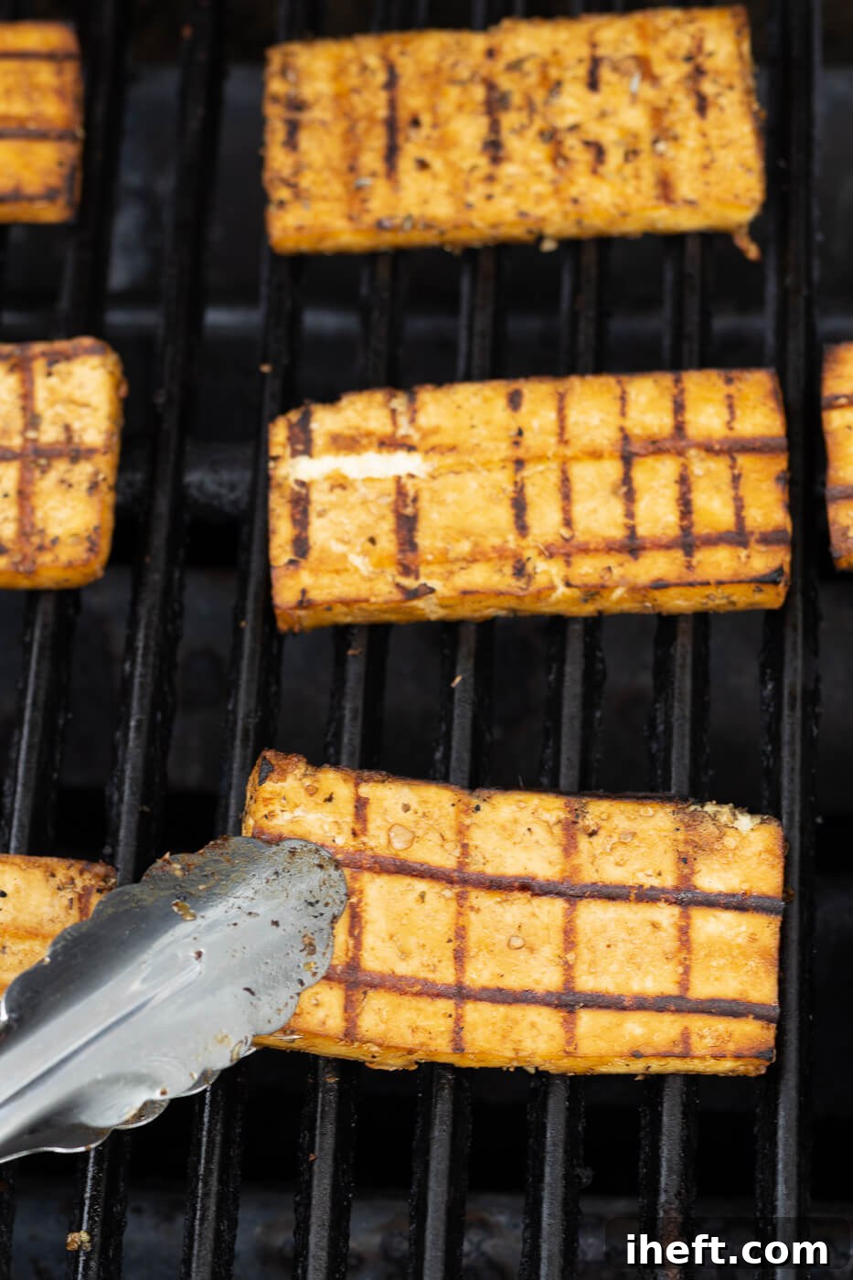 Tongs turn tofu steaks on a grill. 