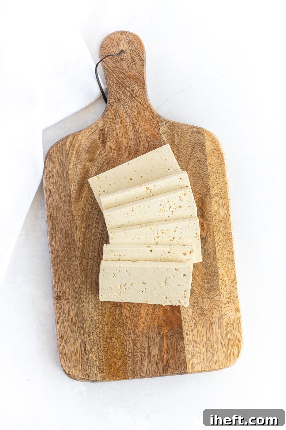 Slices of tofu on a wooden cutting board.