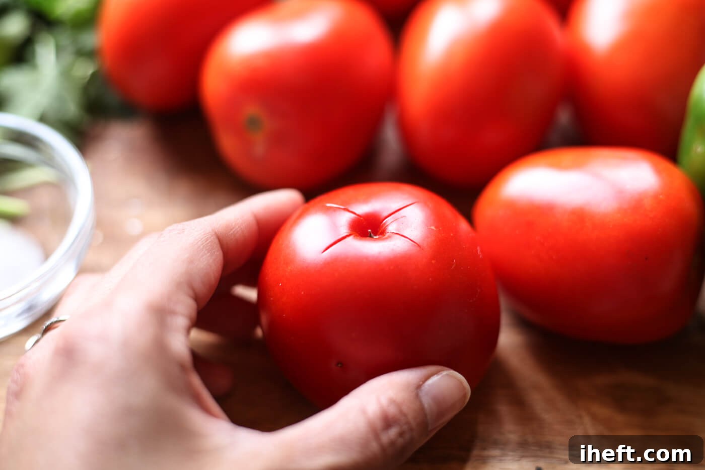 An x is cut into the bottom of a red tomato.