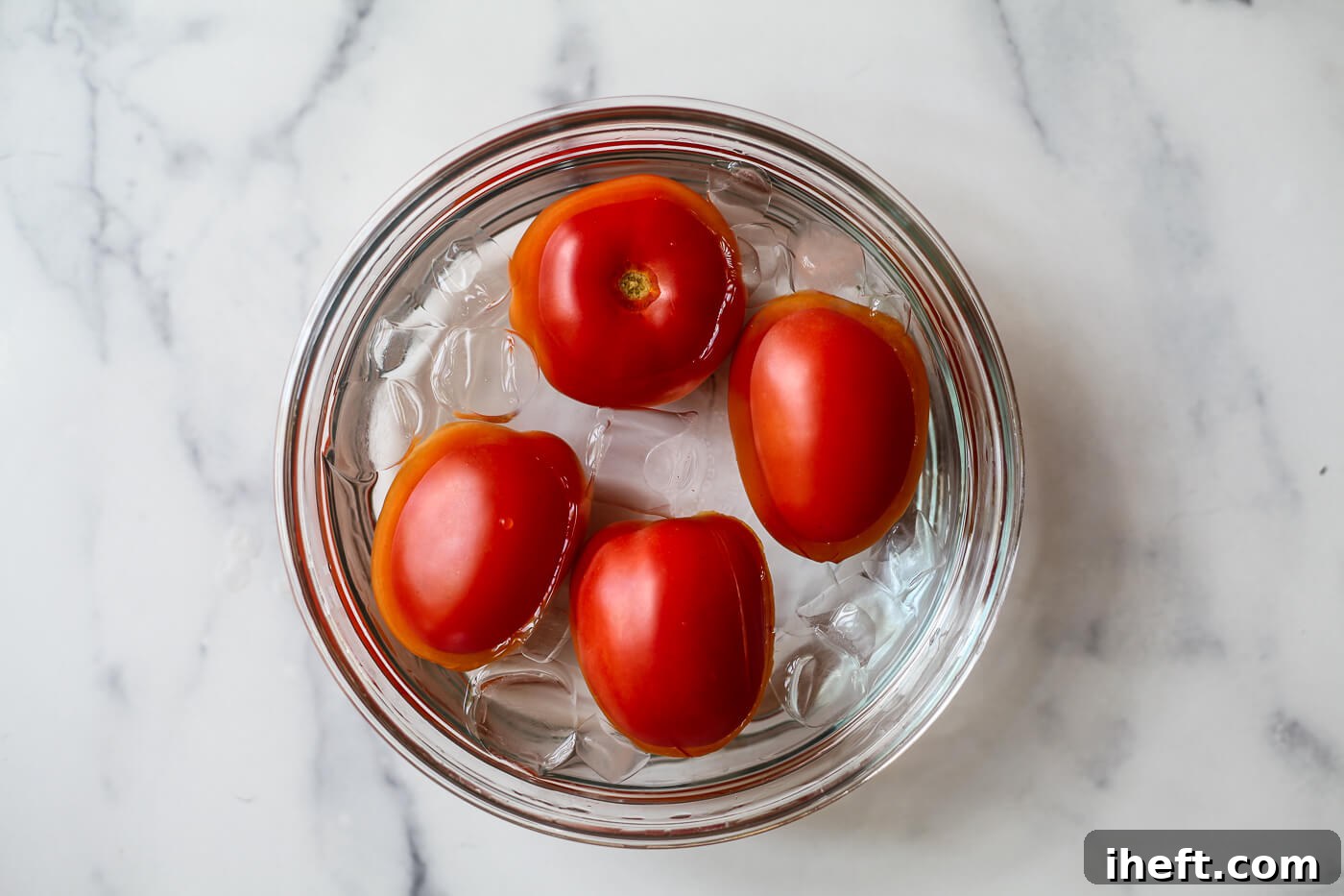 Four Roma tomatoes in a bowl of ice water after boiling.