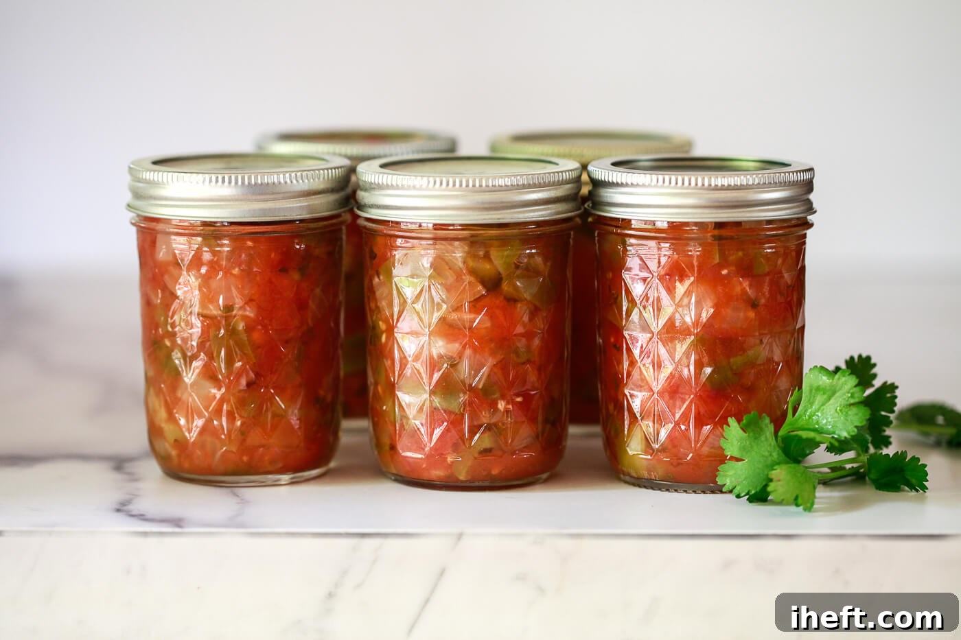 8 oz. Ball jars filled with homemade canned salsa on a marble counter.