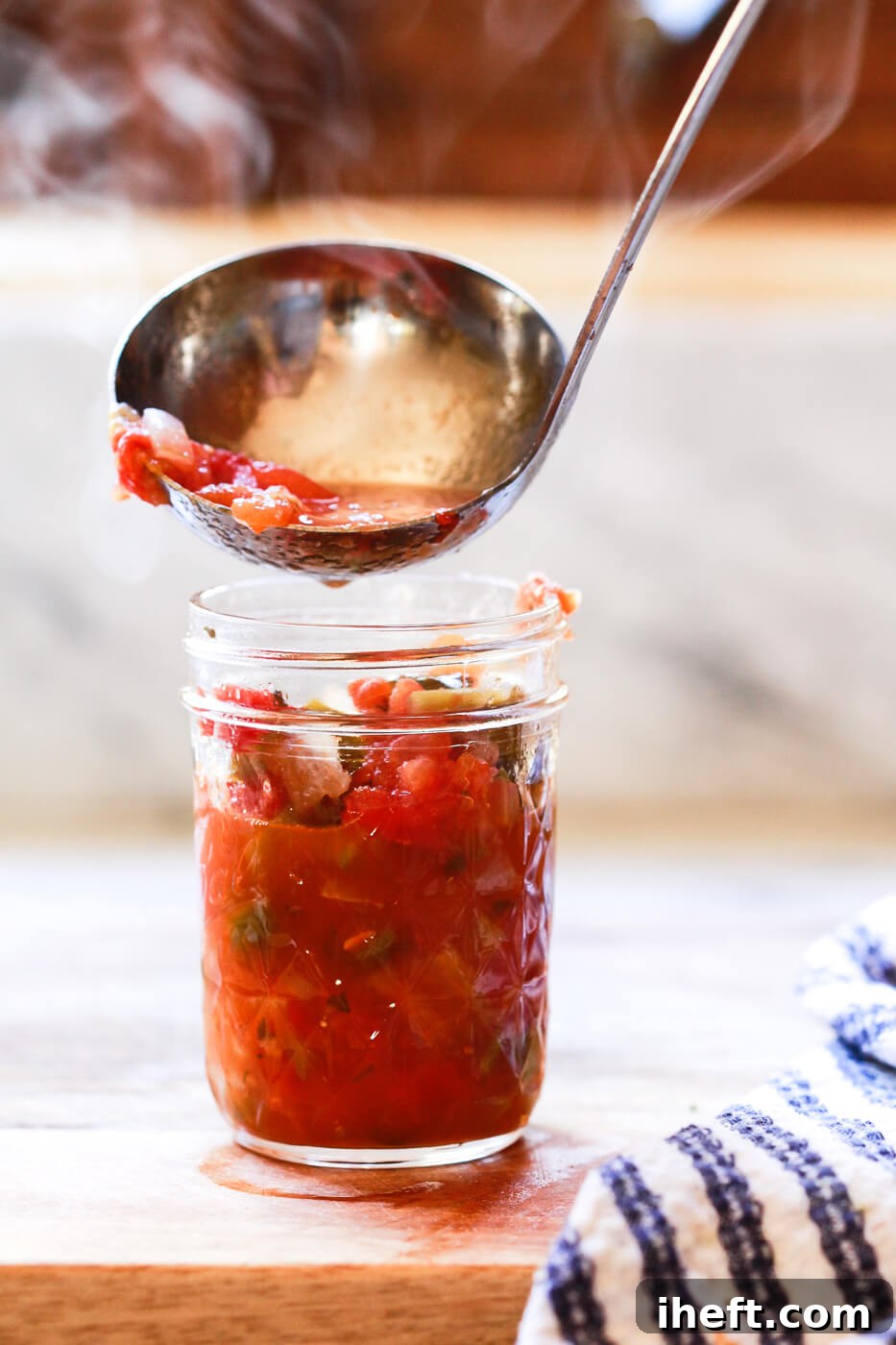 Hot steaming homemade salsa is ladled into a hot Ball mason jar. 