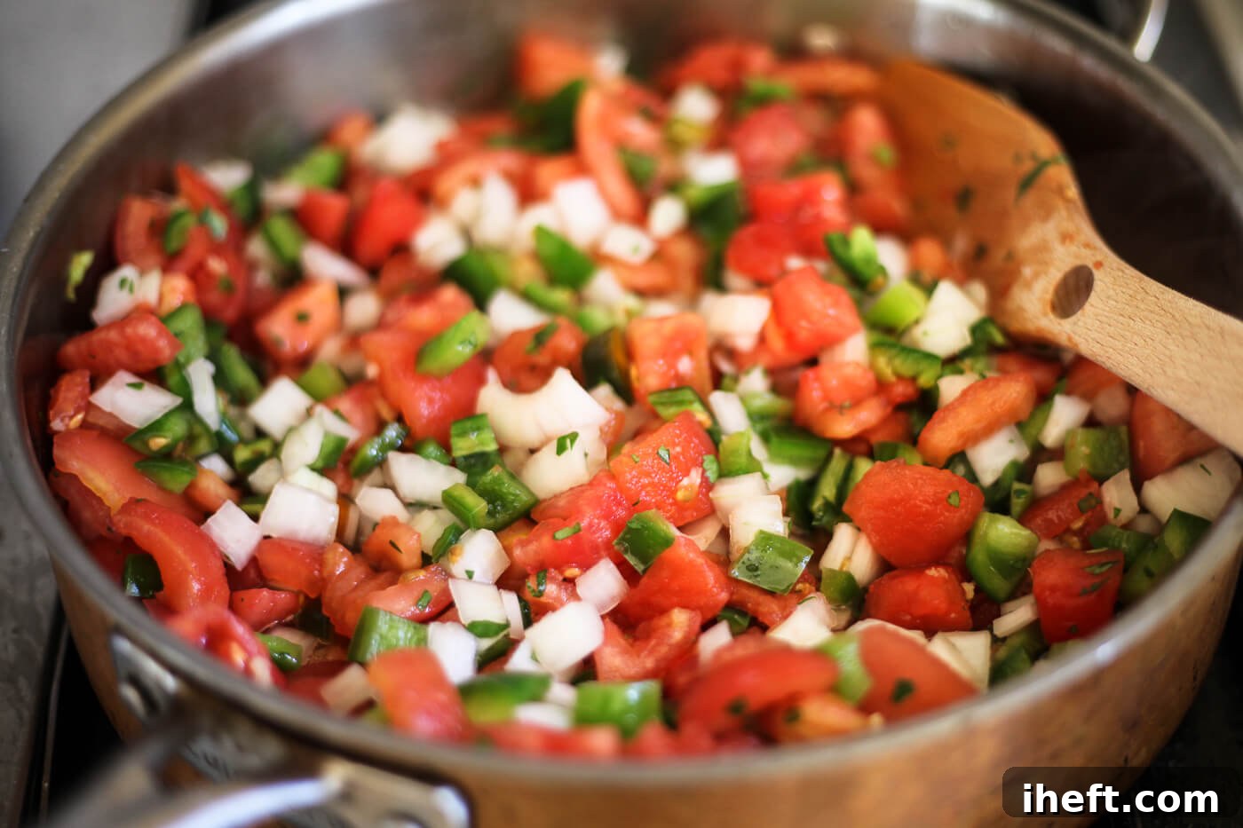 Tomatoes, onions, peppers, and other ingredients are stirred together in a saucepan.
