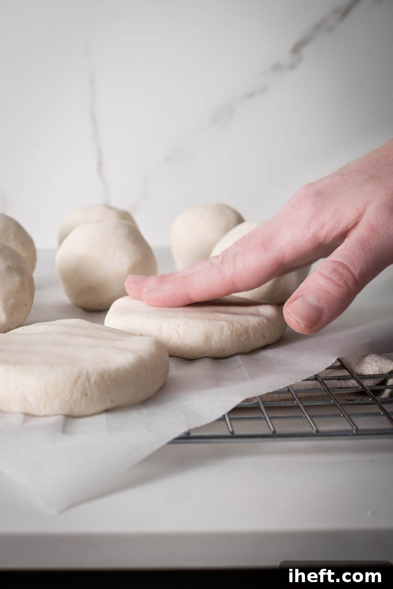 A pair of hands gently pressing a ball of arepa dough into a flat, round disc, illustrating the precise shaping process for achieving uniform arepas.