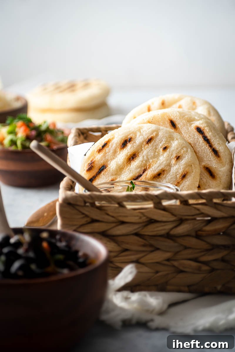 A rustic woven basket overflowing with freshly cooked, golden-brown arepas, accompanied by a small, enticing bowl of rich black beans, symbolizing a classic and comforting Venezuelan meal.