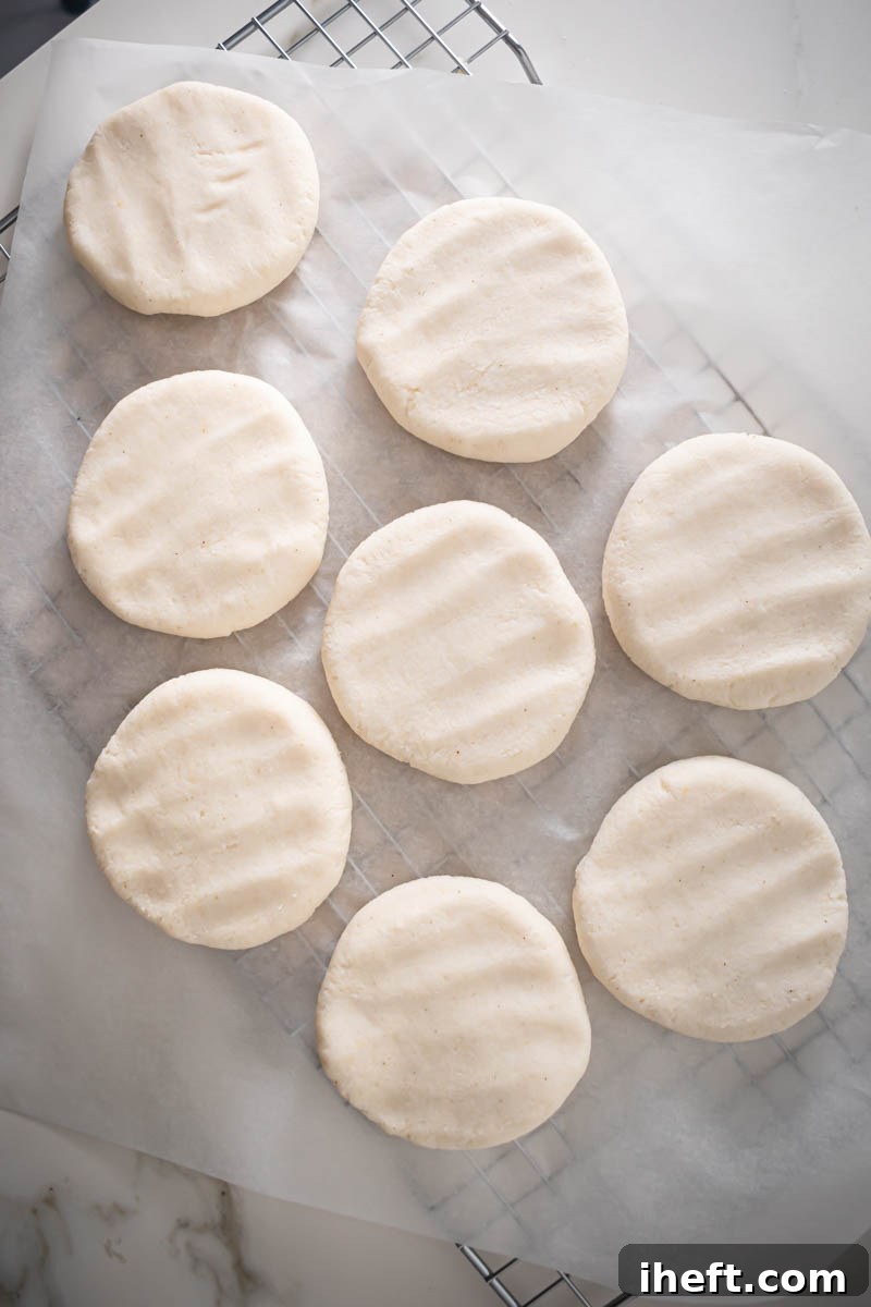 Eight perfectly formed, smooth discs of arepa dough, crafted using Harina P.A.N., are neatly arranged on a piece of parchment paper, ready for grilling, showcasing the ideal consistency before cooking.
