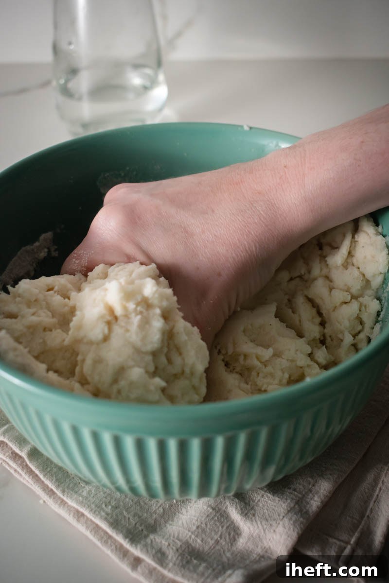 A close-up shot of hands skillfully kneading a smooth and pliable mixture of corn flour, water, and salt in a bowl, demonstrating the correct dough consistency for authentic arepas.