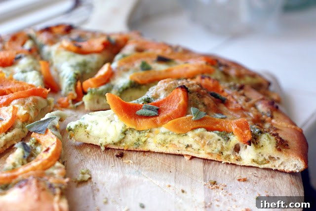 Close-up of a slice of butternut squash pizza, highlighting the roasted squash, melted cheese, and fresh sage.