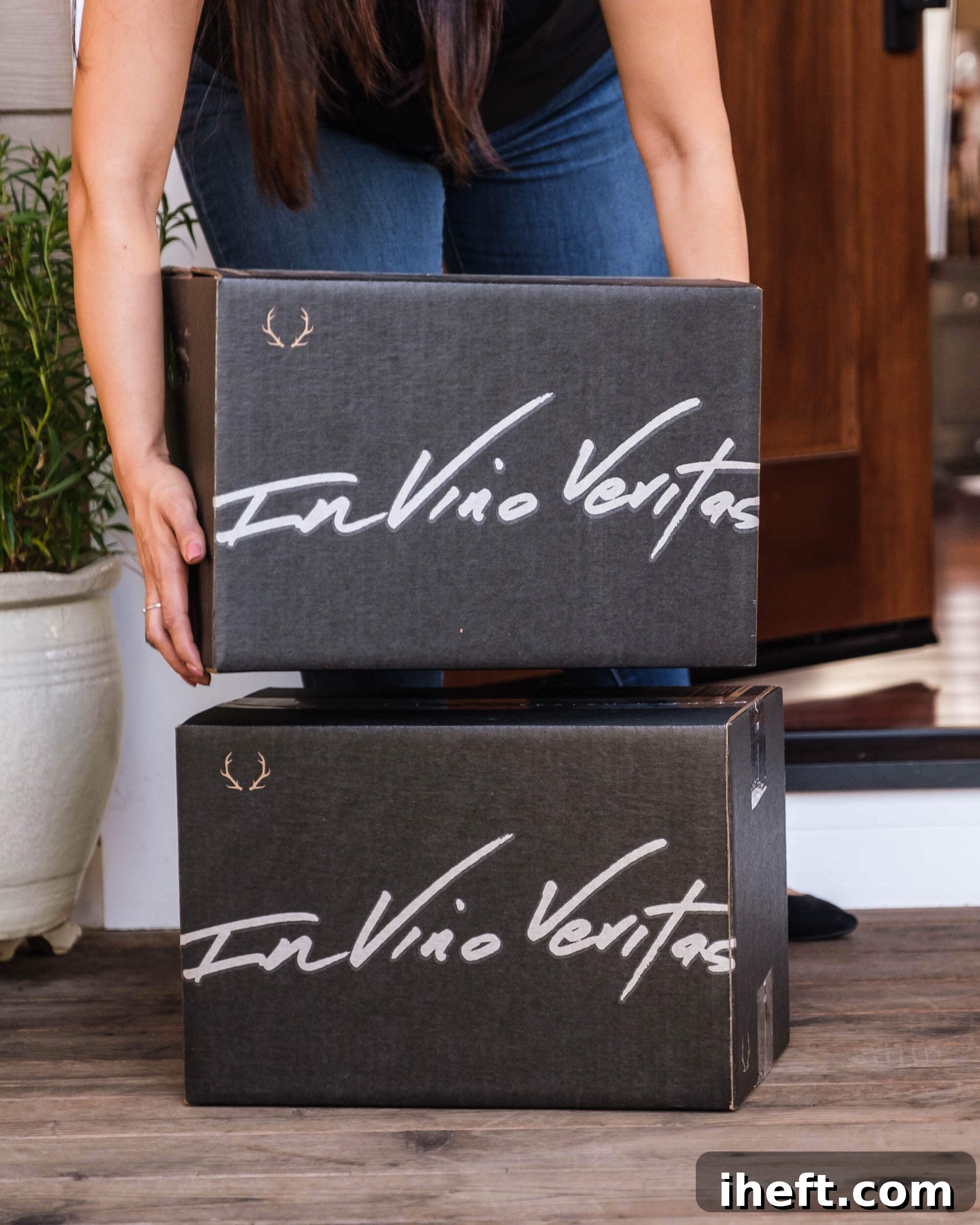 A woman enthusiastically picks up a securely packaged box from Dry Farm Wines from her porch. The boxes are elegantly branded with the Latin phrase 