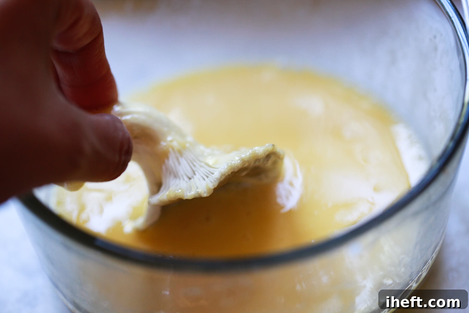 An oyster mushroom being dipped and coated in the egg wash mixture, preparing it for breading.