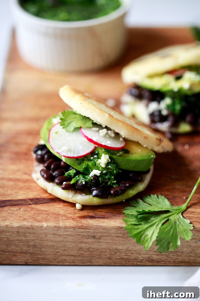 An appetizing close-up of a perfectly cooked arepa, generously filled with savory black beans, melted cheese, and fresh avocado slices.
