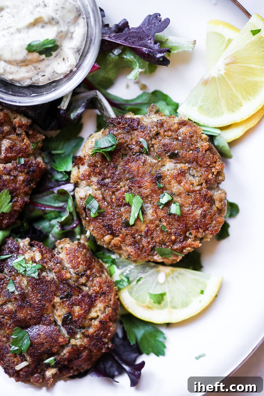 Vegan Crab Cakes perfectly cooked on a plate, served with a delicate sauce, fresh greens, and bright lemon slices for garnish.