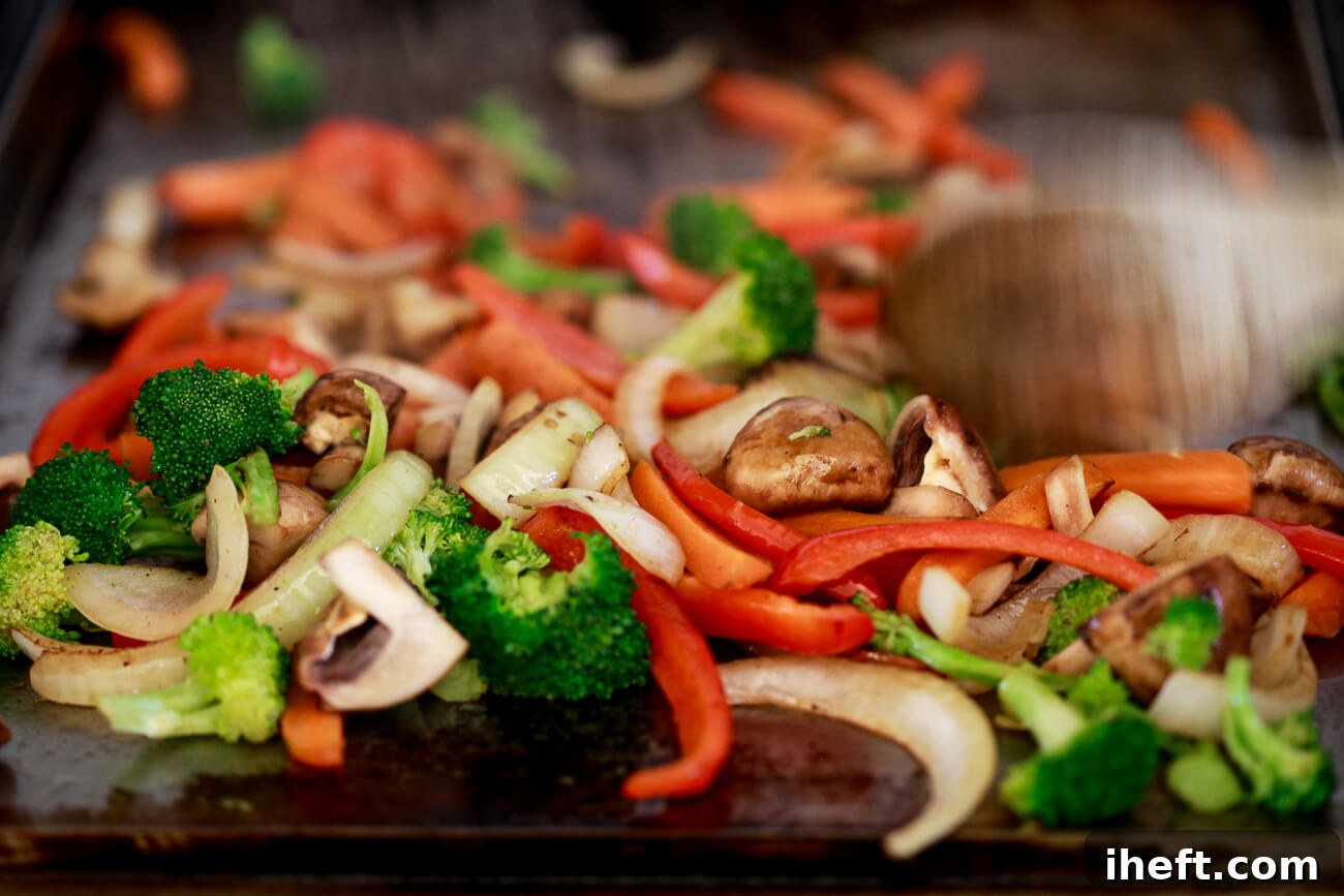 A wooden spoon actively moves stir fry vegetables around a hot flat top griddle, ensuring even cooking.