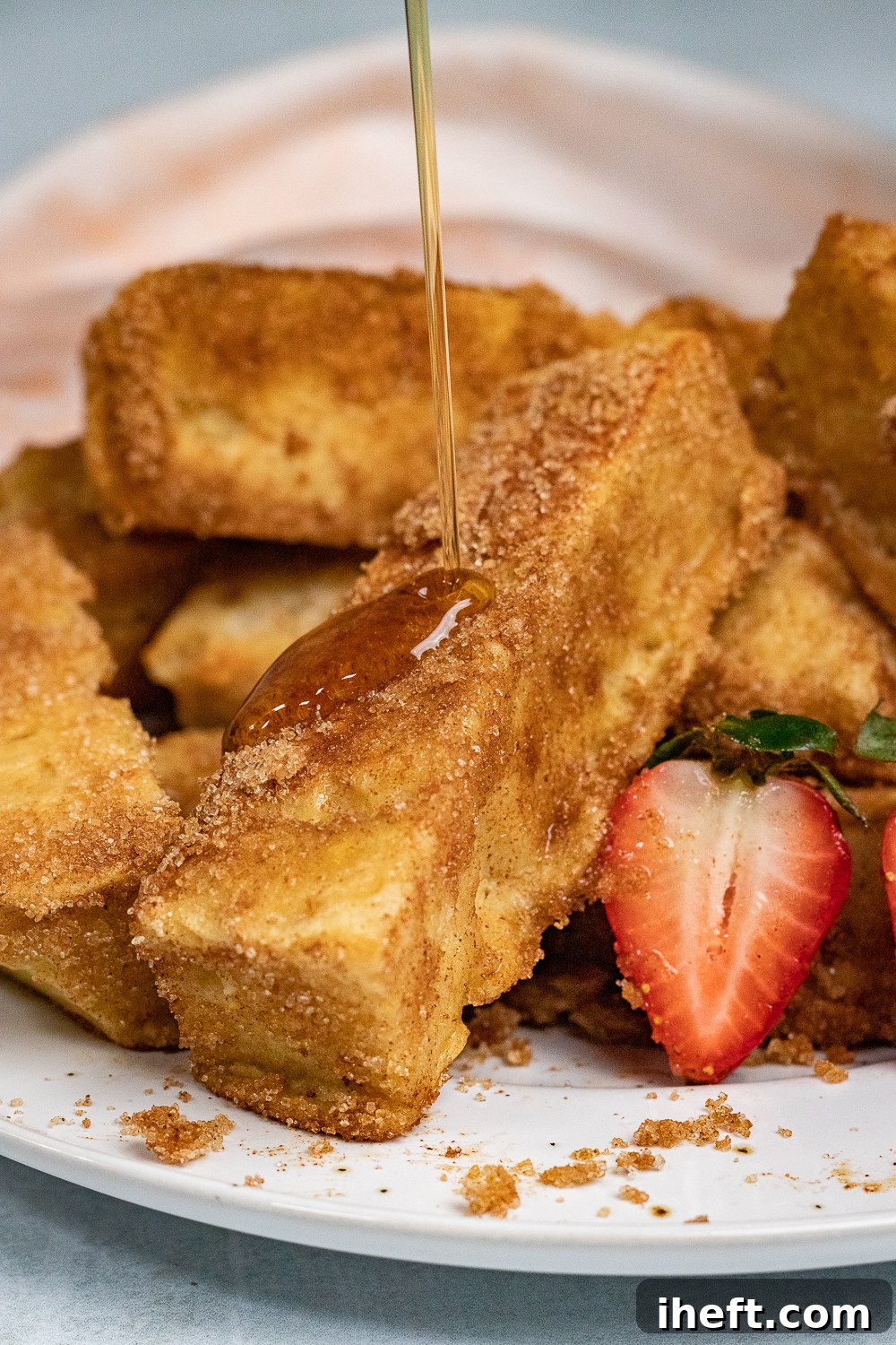 Rich maple syrup generously drizzled over a platter of cinnamon sugar-crusted Vegan French Toast Sticks, perfectly cooked on a griddle.