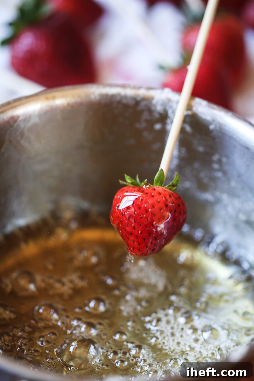 A skewered strawberry is dipped into hot sugar and water to make Tanghulu strawberries.