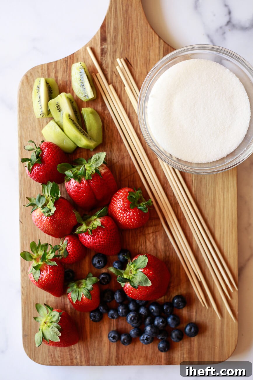 A cutting board topped with strawberries, blueberries, kiwi slices, bamboo skewers, and a bowl of sugar.