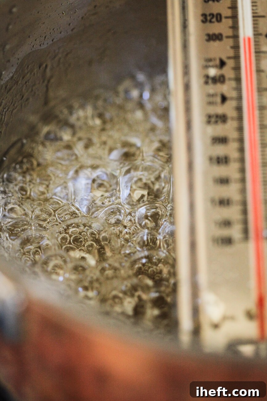 A close-up photo of boiling sugar and water with a candy thermometer that registers 300 degrees F, or Hard Crack stage.