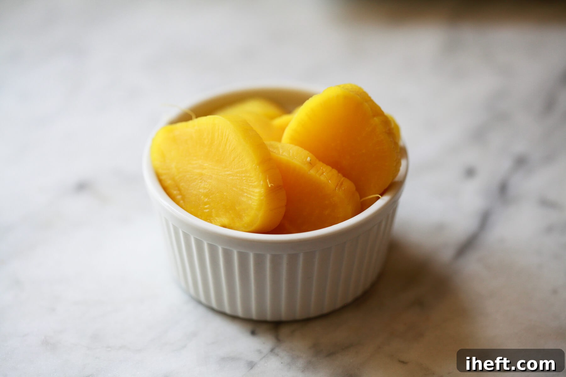 A small white ramekin filled with bright yellow rounds of sliced oshinko (pickled daikon radish), ready to be enjoyed.