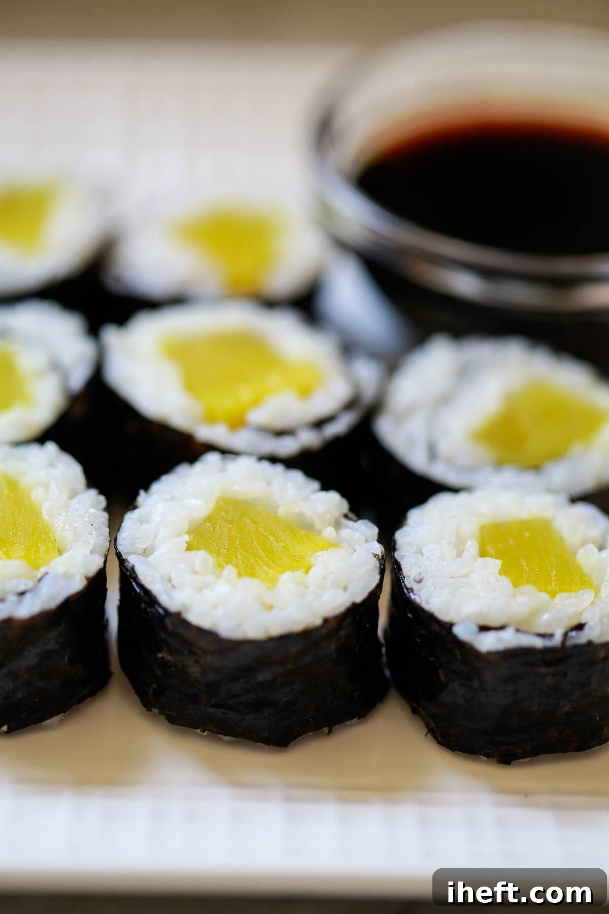 Beautifully arranged oshinko maki sushi rolls on a pristine white plate, with a small dish of soy sauce subtly blurred in the background, ready for a delightful meal.