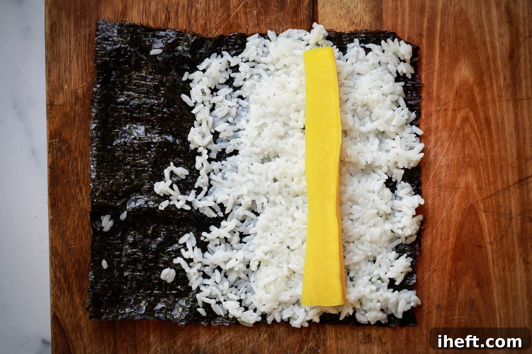 A nori sheet partially covered with fluffy sushi rice, with a perfectly placed piece of oshinko on top, ready for rolling.