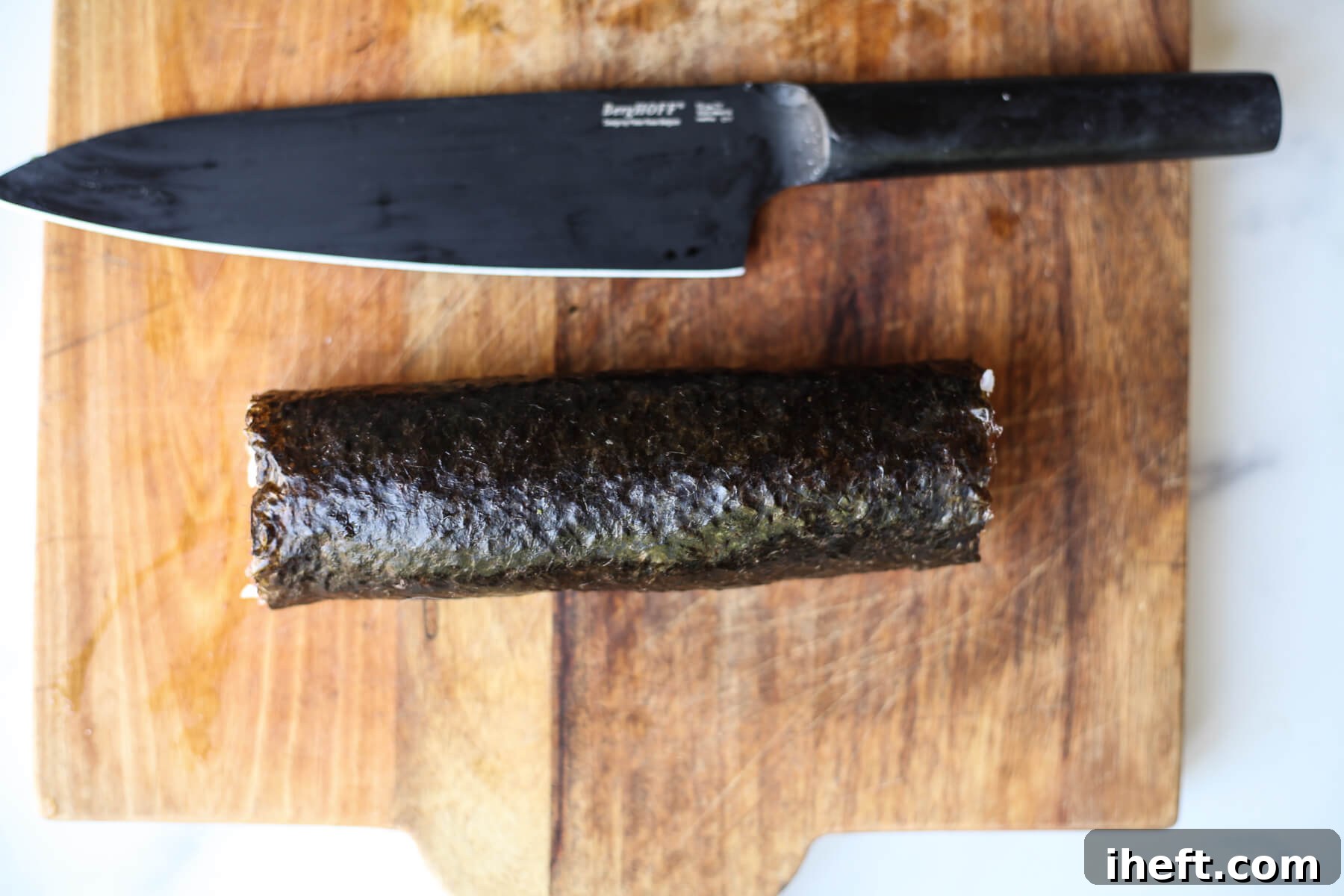 A freshly rolled sushi log rests on a cutting board, positioned next to a sharp knife, awaiting its transformation into individual slices.