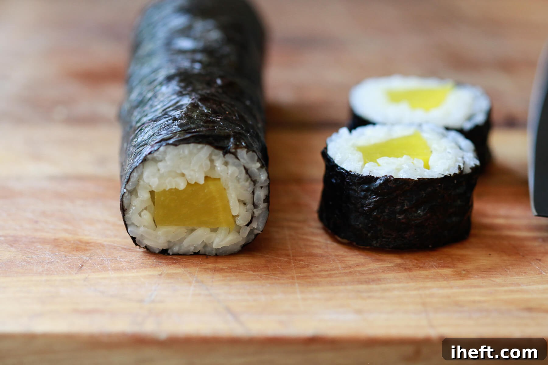 A skilled hand meticulously cutting an oshinko sushi roll into perfectly uniform slices, revealing its colorful interior.