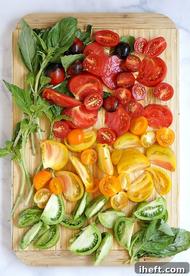 A vibrant and colorful assortment of red, yellow, and green heirloom tomatoes, freshly sliced and artfully arranged, poised to be integrated into a large, healthy kale salad. Accompanied by fragrant green basil leaves, emphasizing freshness.