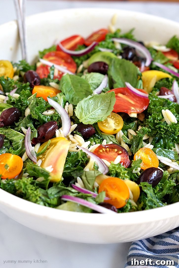 A vibrant close-up of a healthy and visually appealing kale salad, generously mixed with colorful heirloom tomatoes, perfectly cooked orzo pasta, briny Kalamata olives, and thinly sliced red onion, all coated in a delicious dressing.