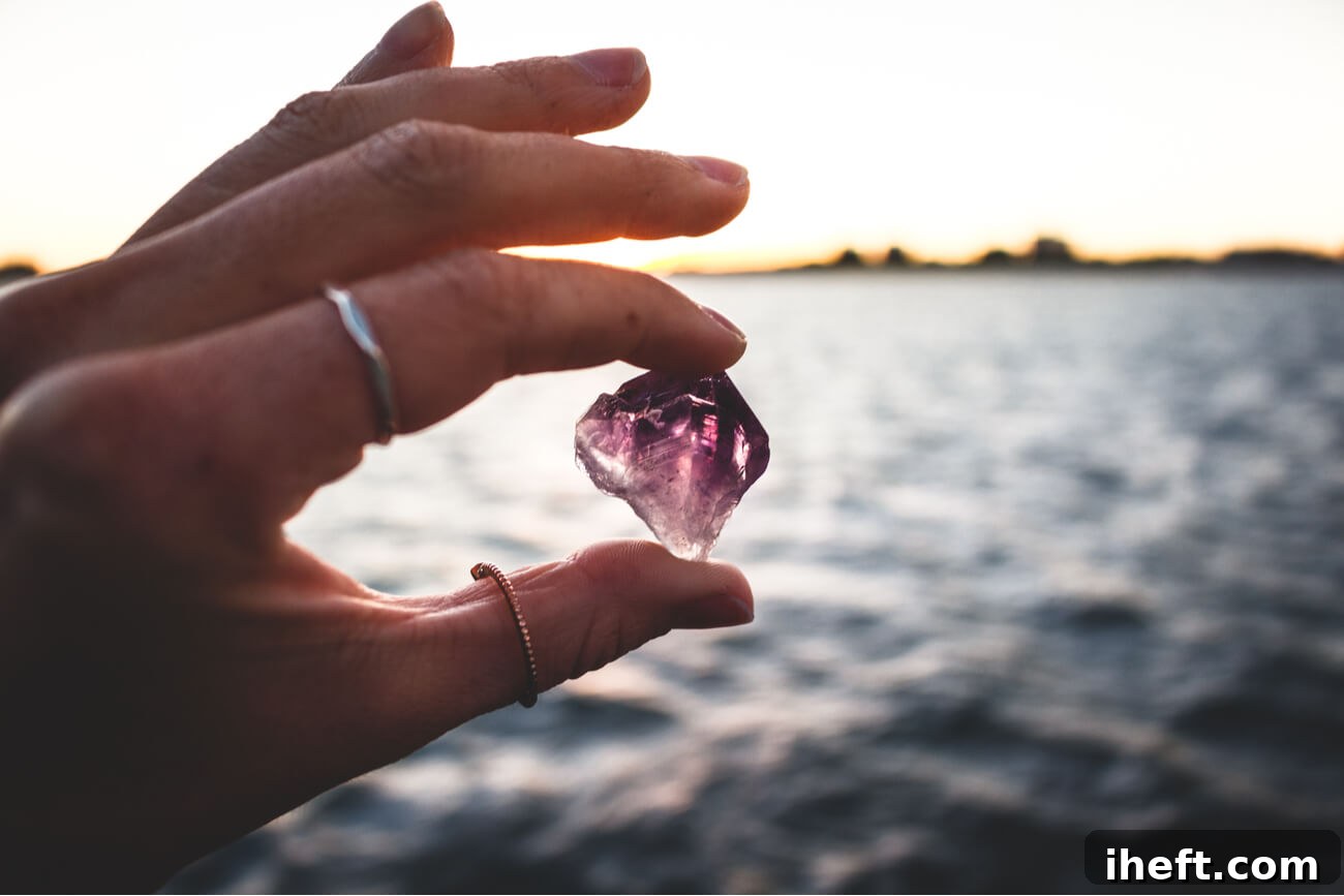 A woman's hand gently holds an amethyst crystal against the backdrop of a vast, tranquil ocean, symbolizing the connection between crystals and natural elements for cleansing. 