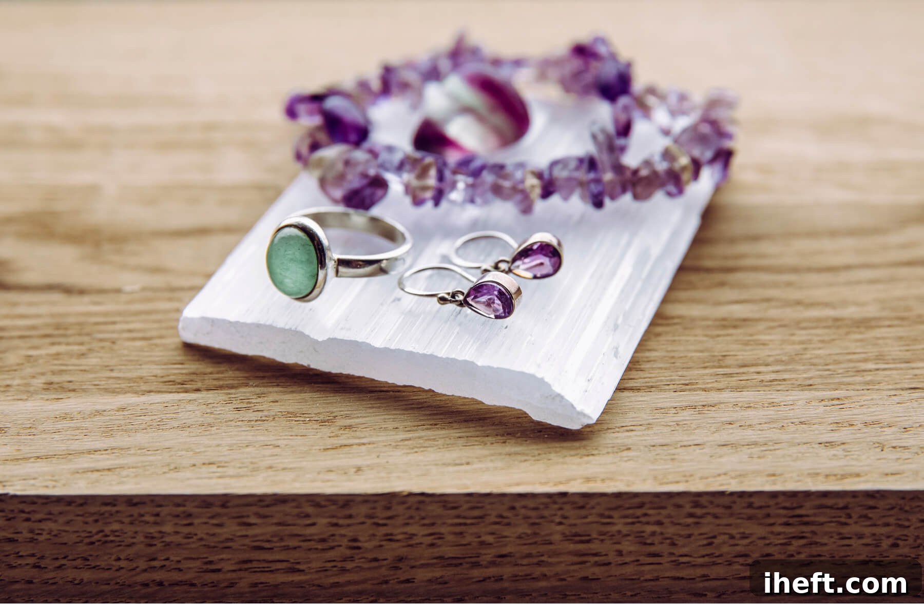 A smooth slab of white Selenite lies on a rustic wooden table, adorned with various pieces of crystal jewelry, illustrating the process of using Selenite for crystal cleansing and charging.