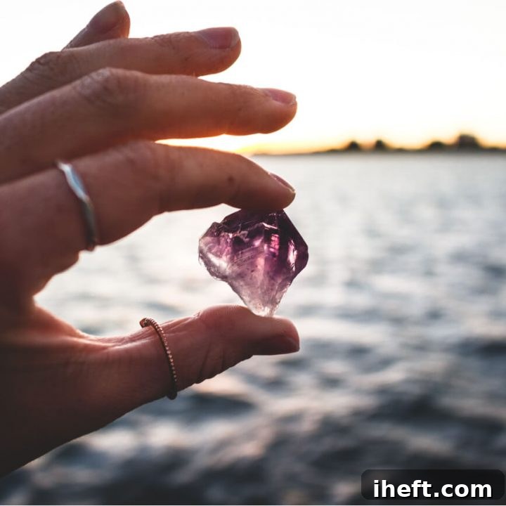 A woman's hand holds an amethyst crystal in front of the ocean. 