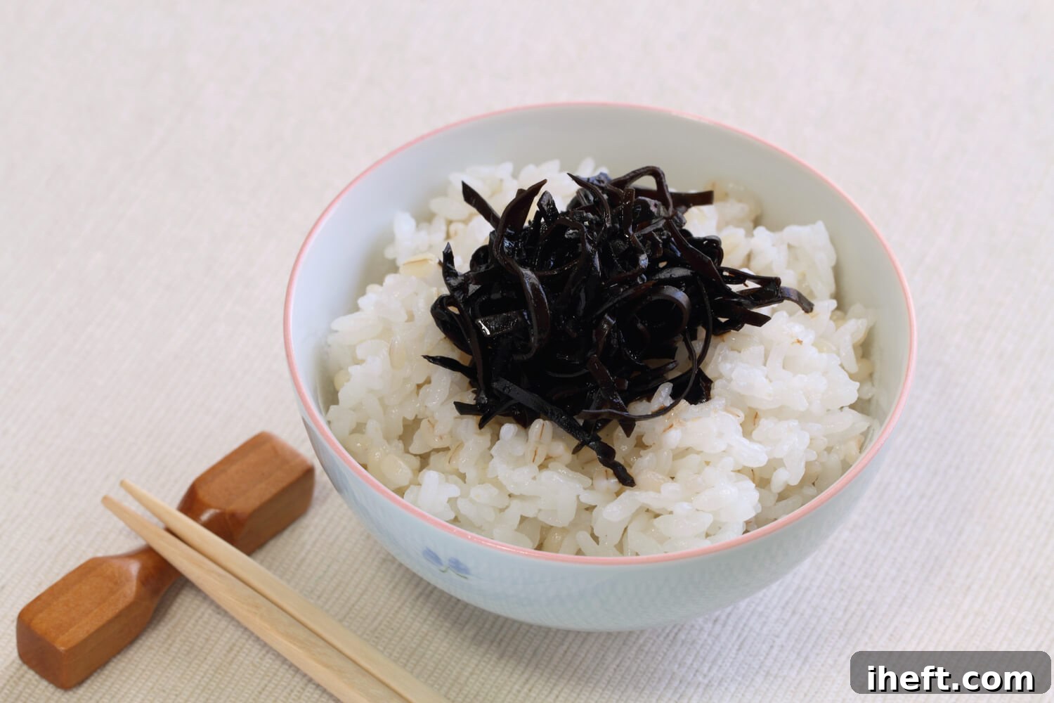 A bowl of rice is topped with black arame seaweed. Chopsticks sit off to the side. 