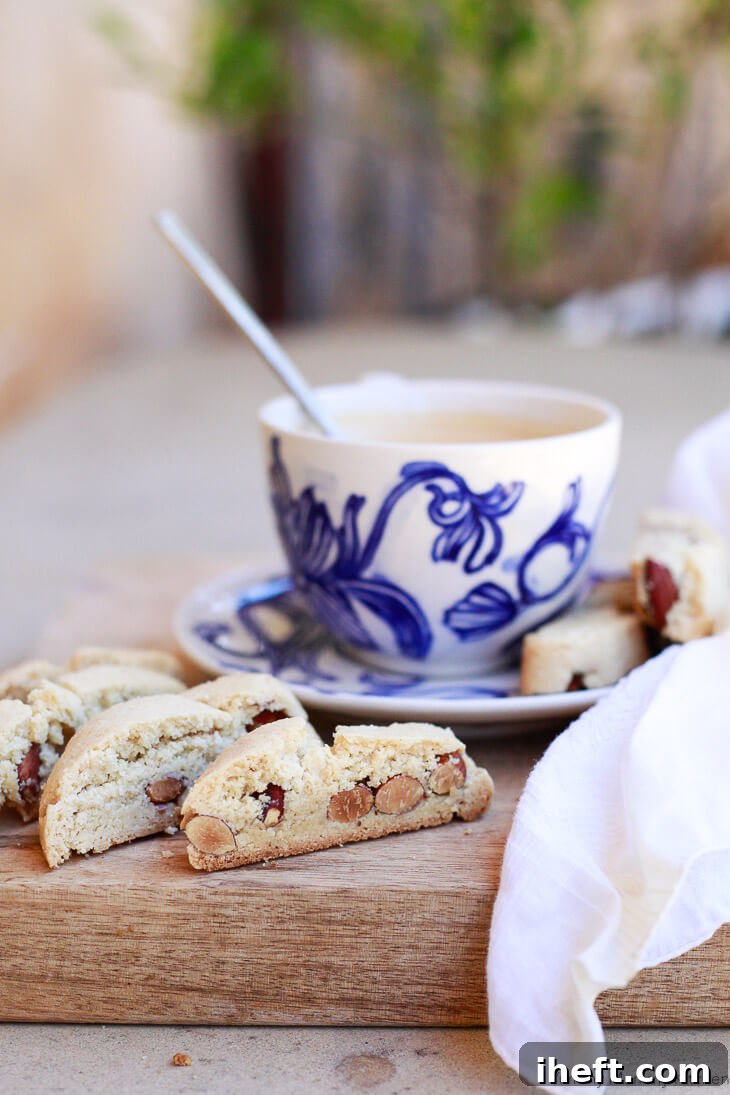 Slices of almond biscotti sit on a cutting board outside with a blue and white tea cup in the background. 
