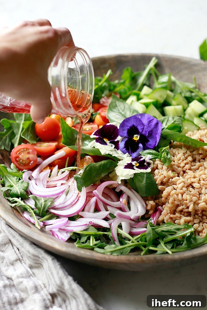 Vinaigrette is poured over a salad of arugula, farro, onions, and tomatoes. 