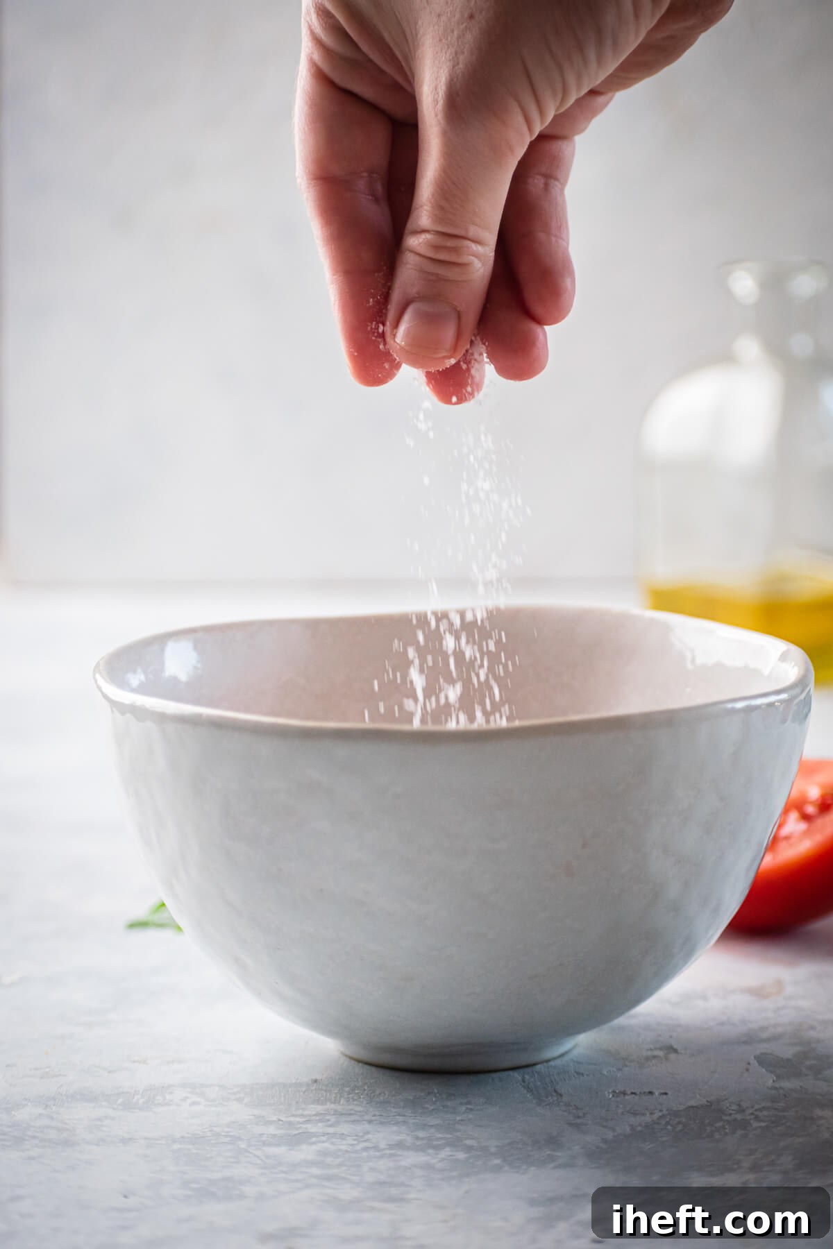 Salt is sprinkled into a small bowl with grated tomato and olive oil.