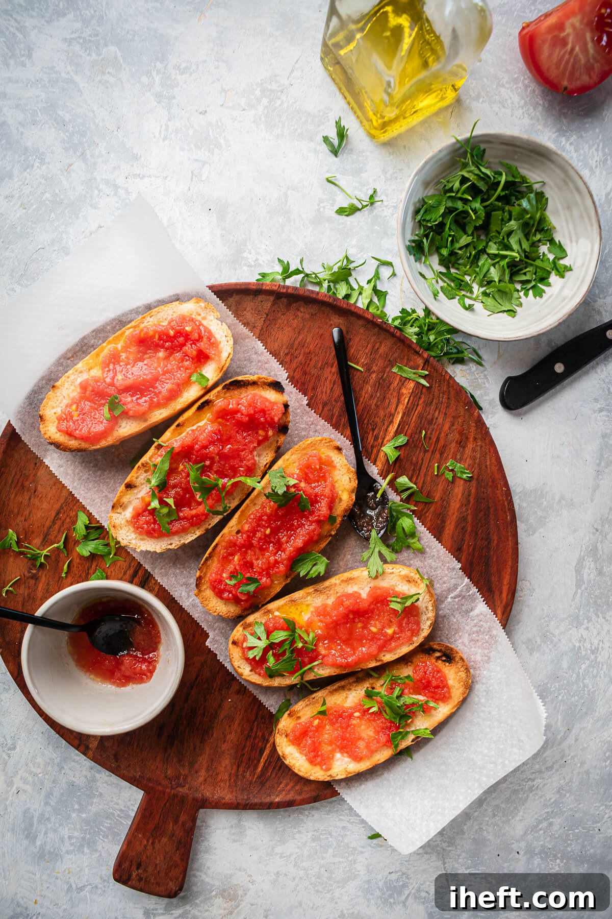 A beautiful overhead photo of 5 pieces of pan con tomate on a wood cutting board on a light grey background.