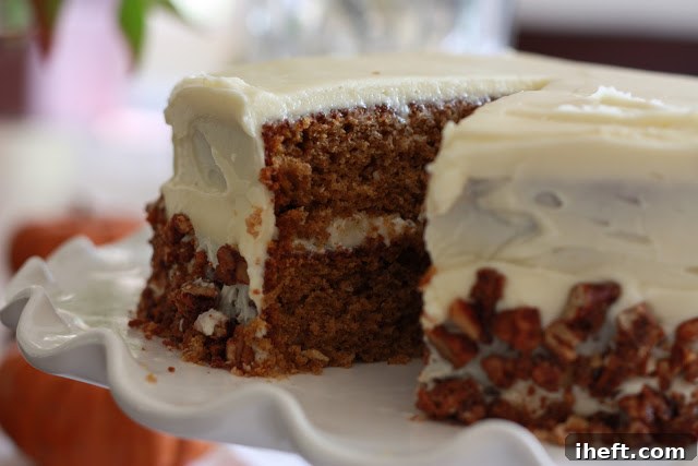 A generous slice of moist pumpkin cake, topped with creamy white cream cheese frosting and crunchy candied pecans.