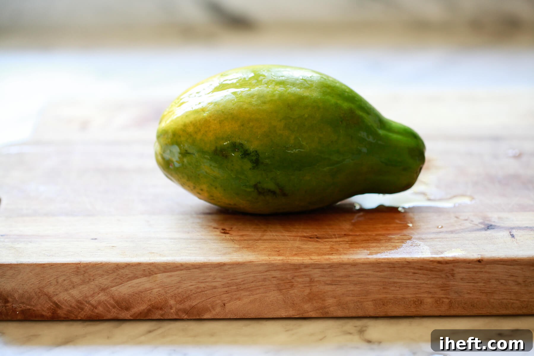 A vibrant green and yellow Hawaiian papaya rests on a natural wooden cutting board, indicating it's reaching optimal ripeness.